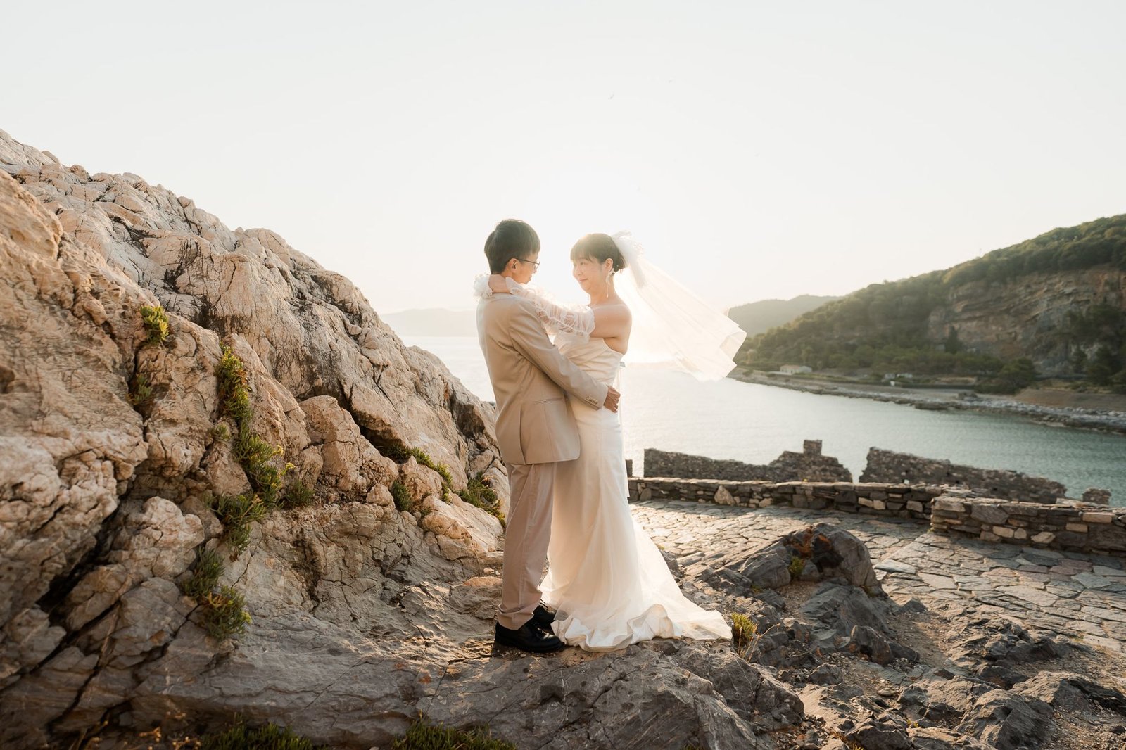 Erica and Lam embrace on the rocks above the bay of Portovenere at golden hour
